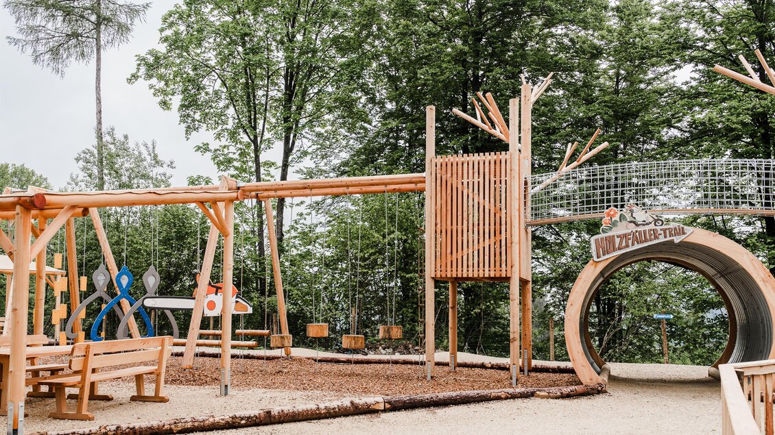 Ein naturnaher Spielplatz aus Holz mit verschiedenen Spielgeräten. Umgeben von Bäumen bietet er eine einladende Umgebung für Kinder. | © Waldpark Hochreiter