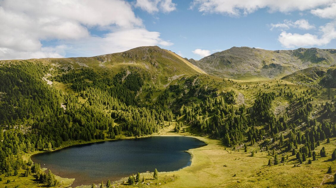 Ein ruhiger Bergsee umgeben von grünen Wäldern und sanften Hügeln. Der Himmel ist blau und leicht bewölkt. | © Erlebnisregion Murtal