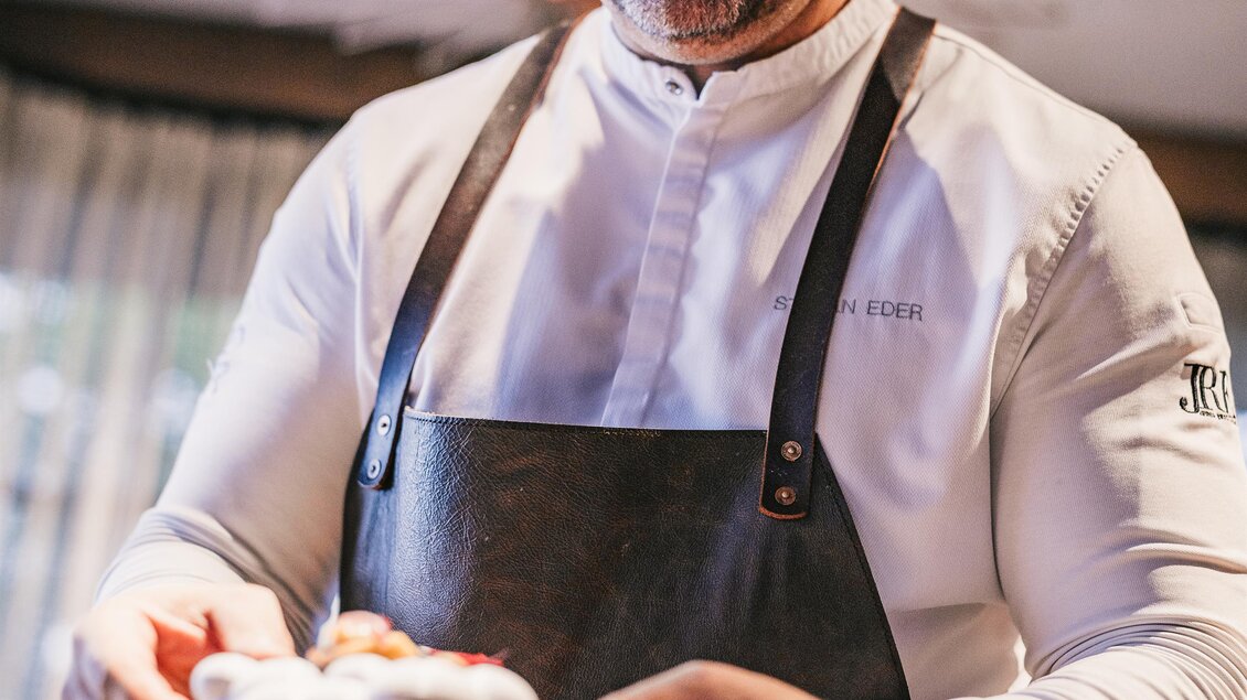 Ein freundlicher Kellner präsentiert ein Gericht in einem stilvollen Restaurant. Der Raum ist hell und gemütlich, mit anderen Gästen im Hintergrund. | © Oststeiermark Tourismus