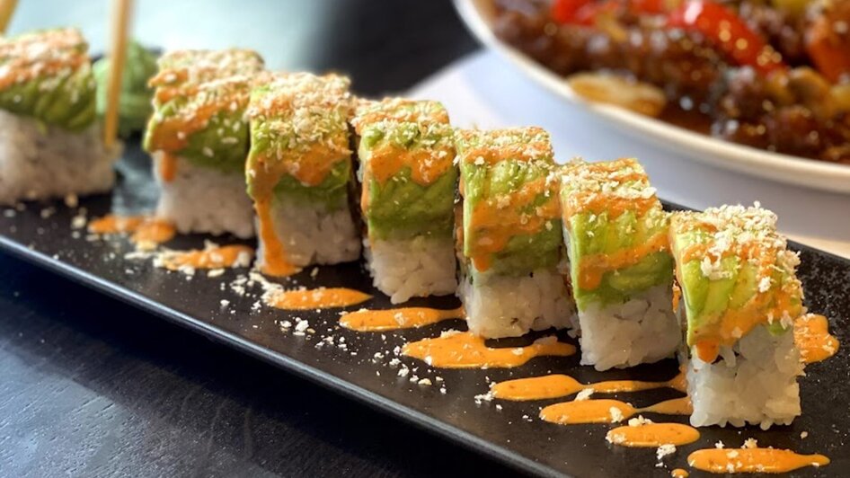 Leckeres Sushi auf einem schwarzen Teller mit Saucen.