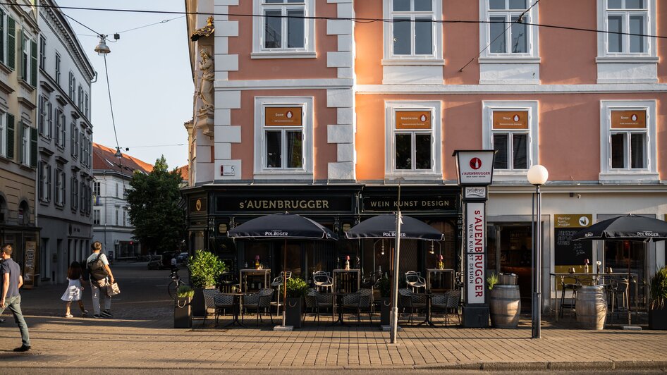 Sicht auf die Auenbrugger Weinbar in Graz, mit Tischen im Freien.