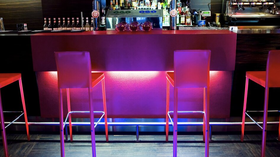 Stylische Bar mit beleuchtenden Stehtischen und Getränkeregalen.