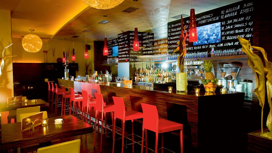 Moderne Bar mit farbigen Stühlen und beleuchteter Theke.