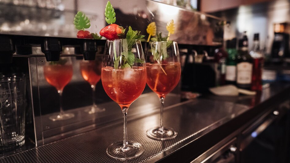 Zwei Cocktails mit Früchten und Kräutern auf einer Bar in einem Café.