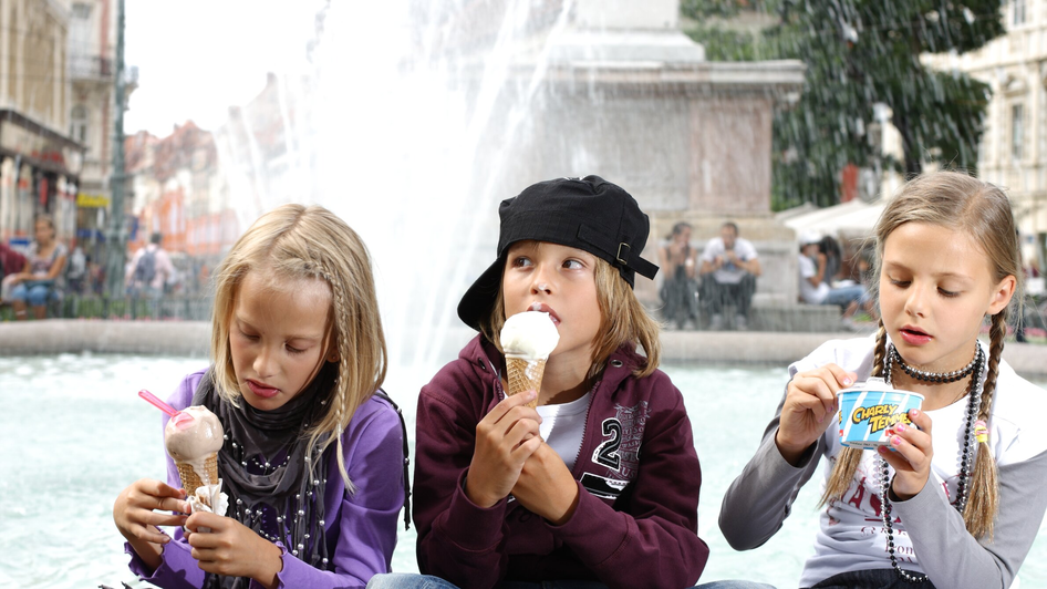 Drei Kinder genießen Eis vor einem Brunnen in Graz.