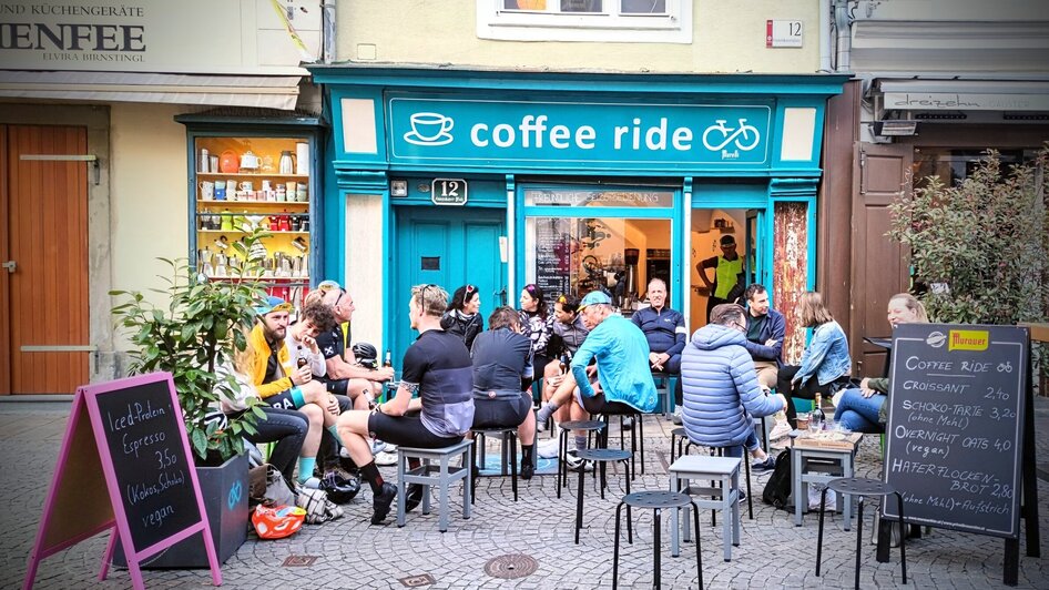 Blick auf das Café 'Coffee Ride' in Graz mit Gästen draußen.