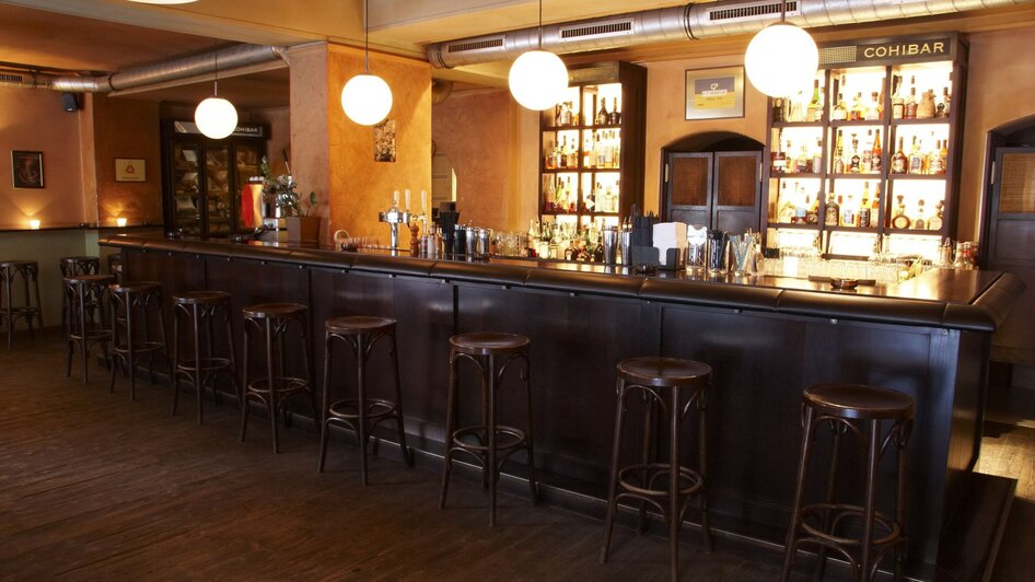 Gemütliche Bar mit Holztheke und großen Leuchten.