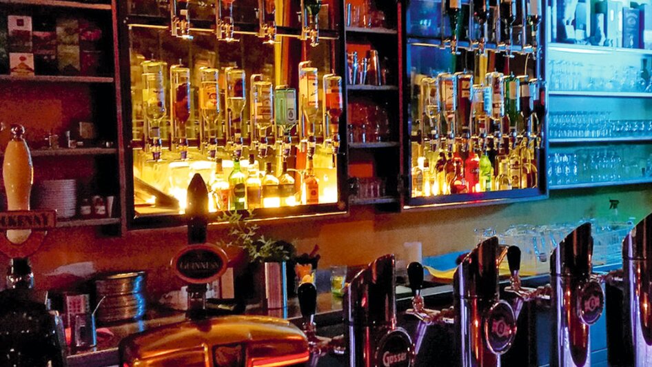 Bar mit einer Vielzahl von Spirituosen und Getränken in warmem Licht.