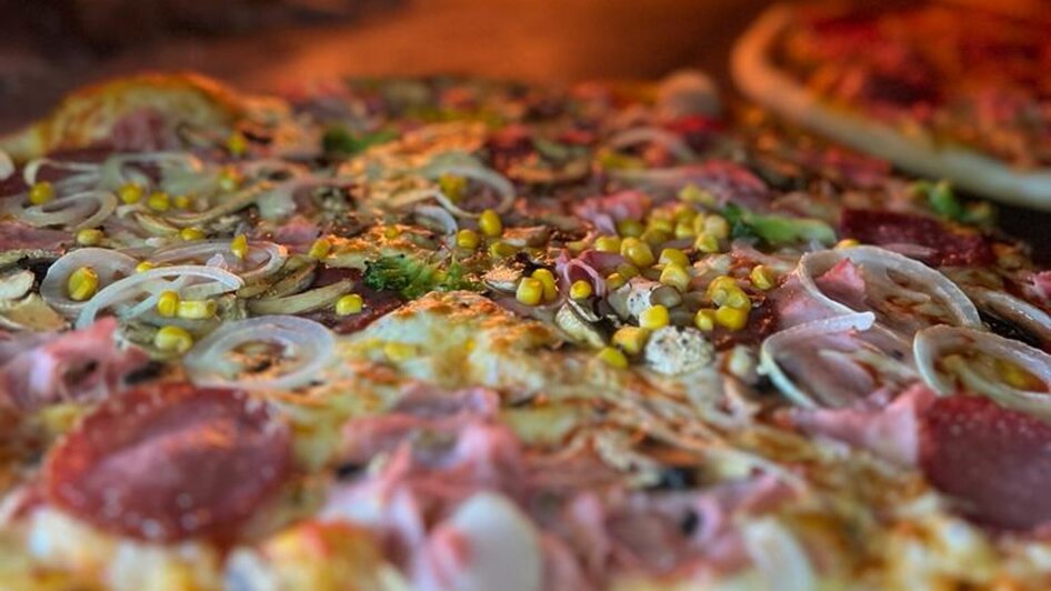 Leckere Pizza wird im Holzofen gebacken, mit Feuer im Hintergrund.