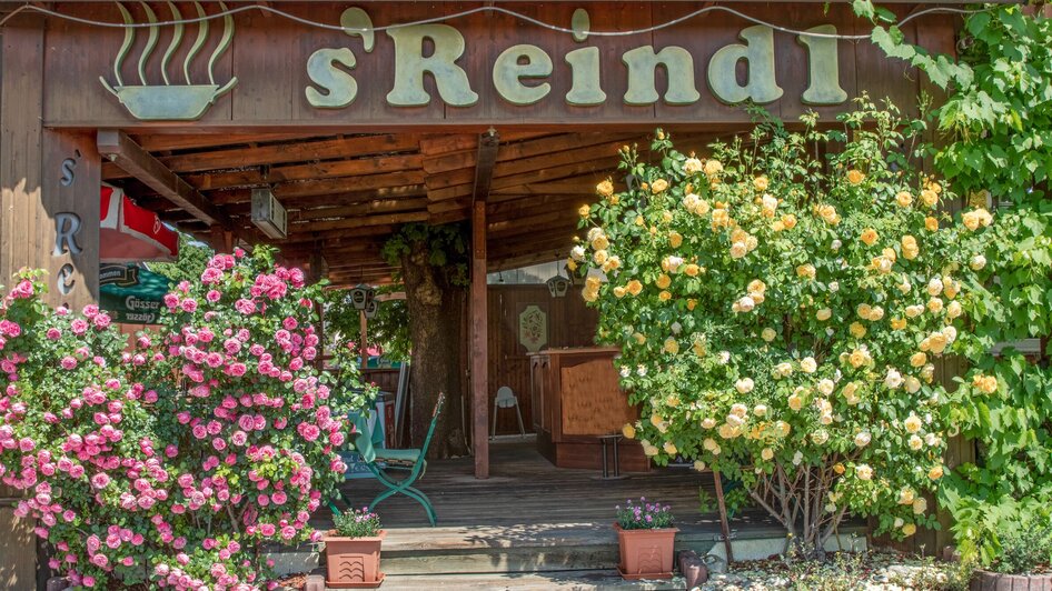 Die Eingangstür des Gasthofs s'Reindl, umgeben von blühenden Pflanzen.