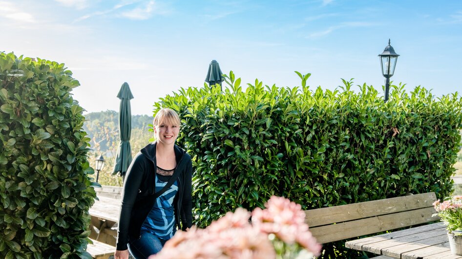Eine lächelnde Frau im Freien, umgeben von Pflanzen und Blumen. | © Graz Tourismus - Mias Photoart
