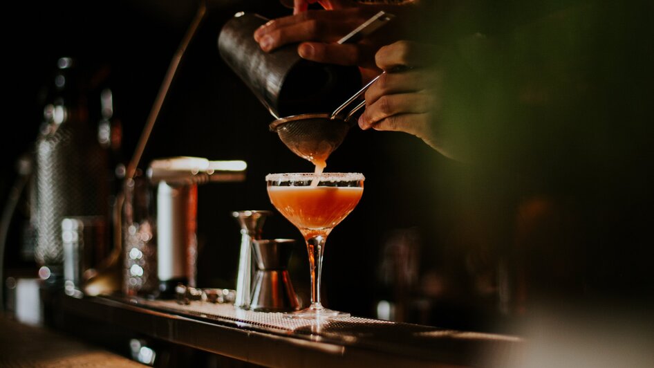 Ein Barkeeper gießt einen Cocktail in ein Glas an einer Bar.