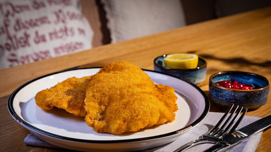 Panierte Schnitzel mit Zitrone und Preiselbeeren auf einem Teller mit Besteck.