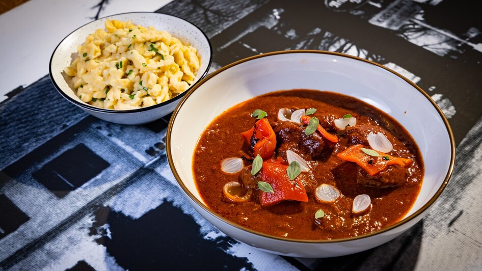 Herzhaftes Gulasch mit Paprika und Nockerl als Beilage, serviert in Graz.