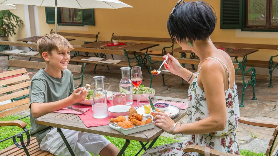 Ein Junge und eine Frau genießen ein Essen im Kreuzwirt am Rosenberg in Graz.