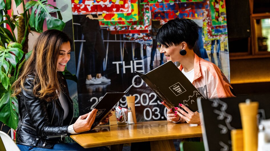 Zwei Frauen im Kunsthauscafé in Graz beim Lesen der Speisekarte.