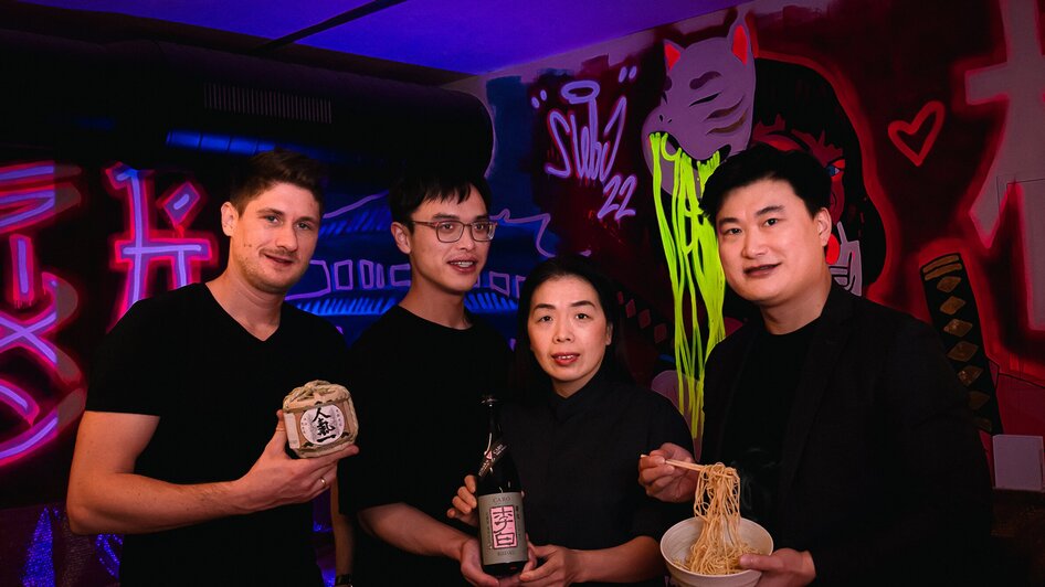 Vier Personen halten Nahrungsmittel und Getränke in einer stylischen Bar.