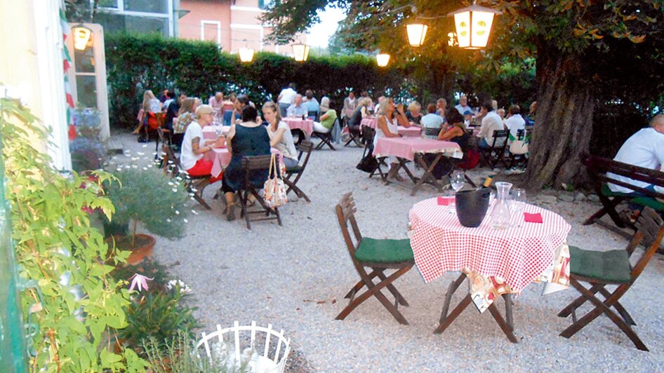 Gemütlicher Gastgarten mit Tischen und Gästen.