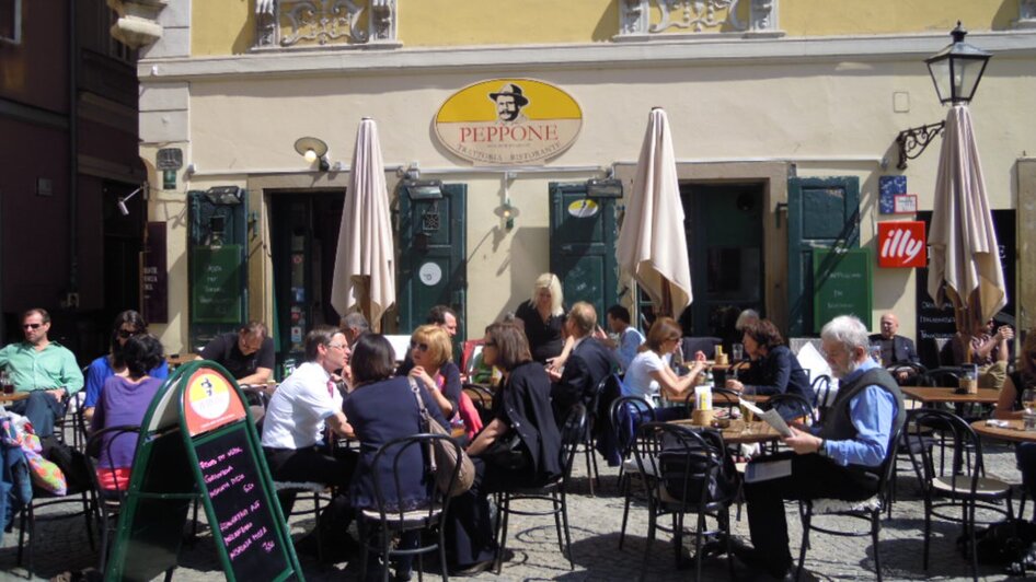 Menschen genießen Speisen und Getränke vor dem Restaurant Peppone in Graz.