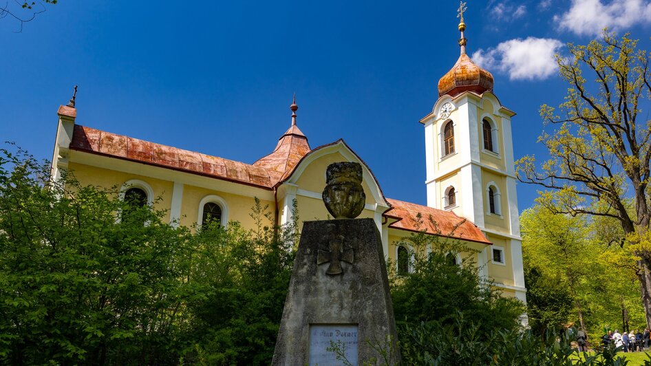 Eine Kirche umgeben von Bäumen und einem Denkmal im Vordergrund.