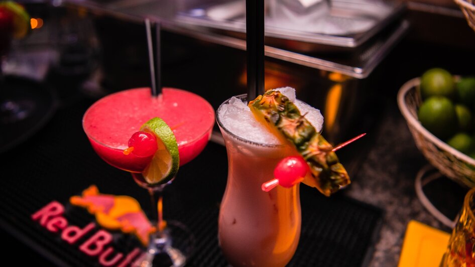 Zwei bunte Cocktails auf einer Bar, einer mit Ananas und der andere mit Limette.