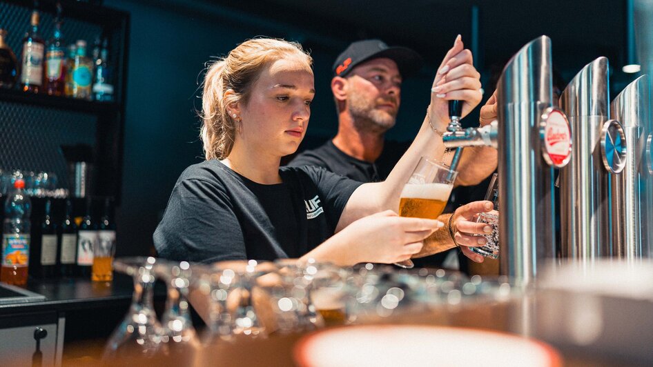 Zwei Personen zapfen Bier an der Bar, eine Frau und ein Mann. | © GEPA I RUFF Golf Graz