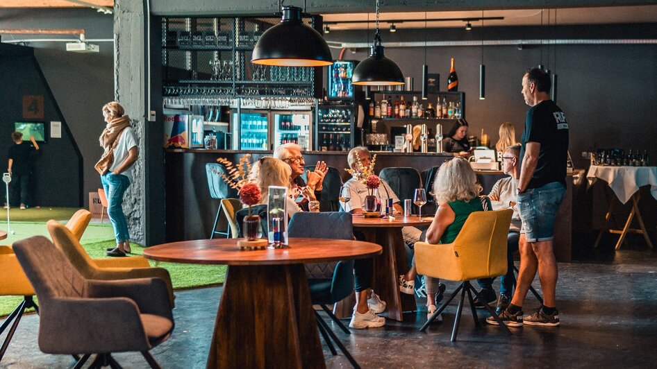Ein gemütlicher Innenraum mit Gästen, die an einem Tisch sitzen, während ein Kellner bedient. | © GEPA I RUFF Golf Graz