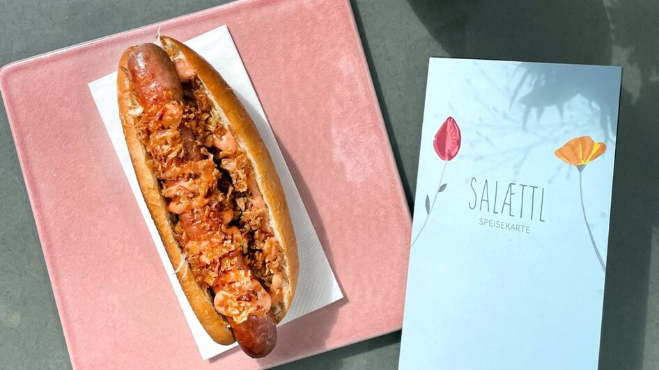 Ein Hotdog auf rosa Platte mit Speisekarte in einem modernen Café.