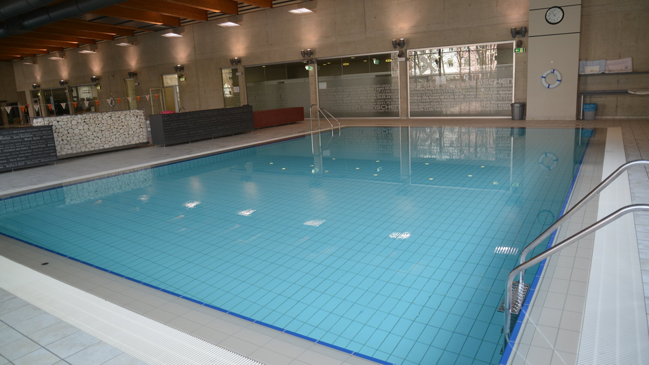 Modernes Hallenbad mit blauem Wasser und Holzdecke.