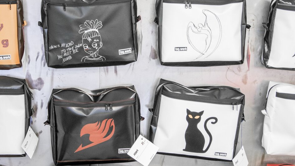 Verschiedene Taschen mit kreativen Designs, darunter Sprüche wie 'Believe in yourself' und Illustrationen.